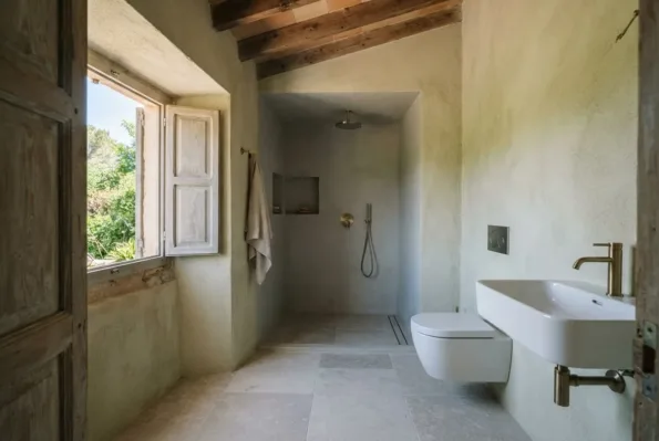 A finished bathroom with a plastered walk-in shower, a wall hung basin and WC, and a shuttered window beside the door.