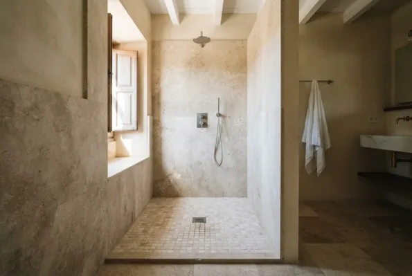 A stone-clad shower recess with small mosaic floor tiles sloping to a central drain, a rain shower head and a hand shower.