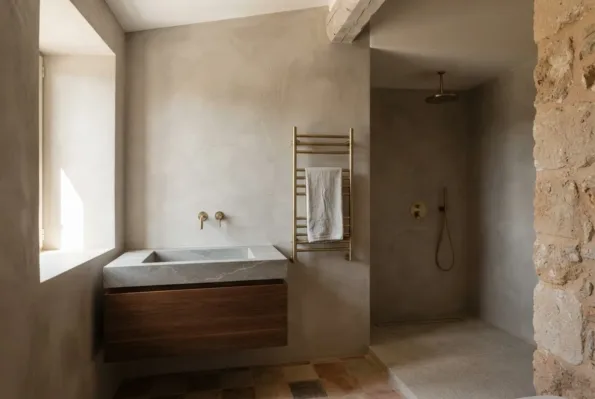A bathroom pairs a stone basin on a dark wood vanity with brass taps and a walk-in shower over terracotta tiles.