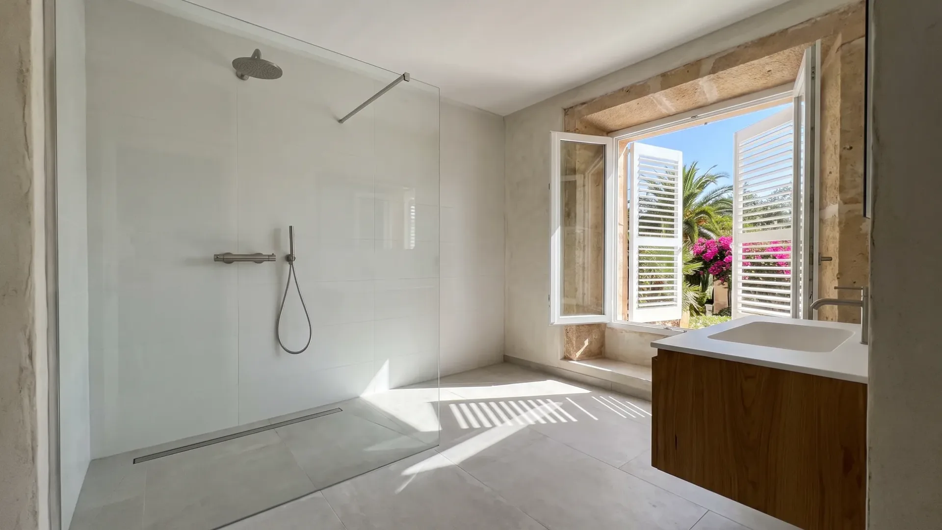 A walk-in glass shower with white tiles opens beside a window framed by palm trees and pink bougainvillea.