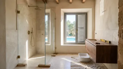 A bathroom under construction has a glass shower screen, travertine tile walls, and an unfitted basin on a wooden vanity.