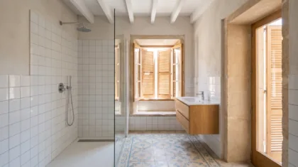 A shower lined in white square tiles sits beside a floating oak vanity on patterned blue and white cement floor tiles.