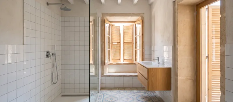 A shower lined in white square tiles sits beside a floating oak vanity on patterned blue and white cement floor tiles.