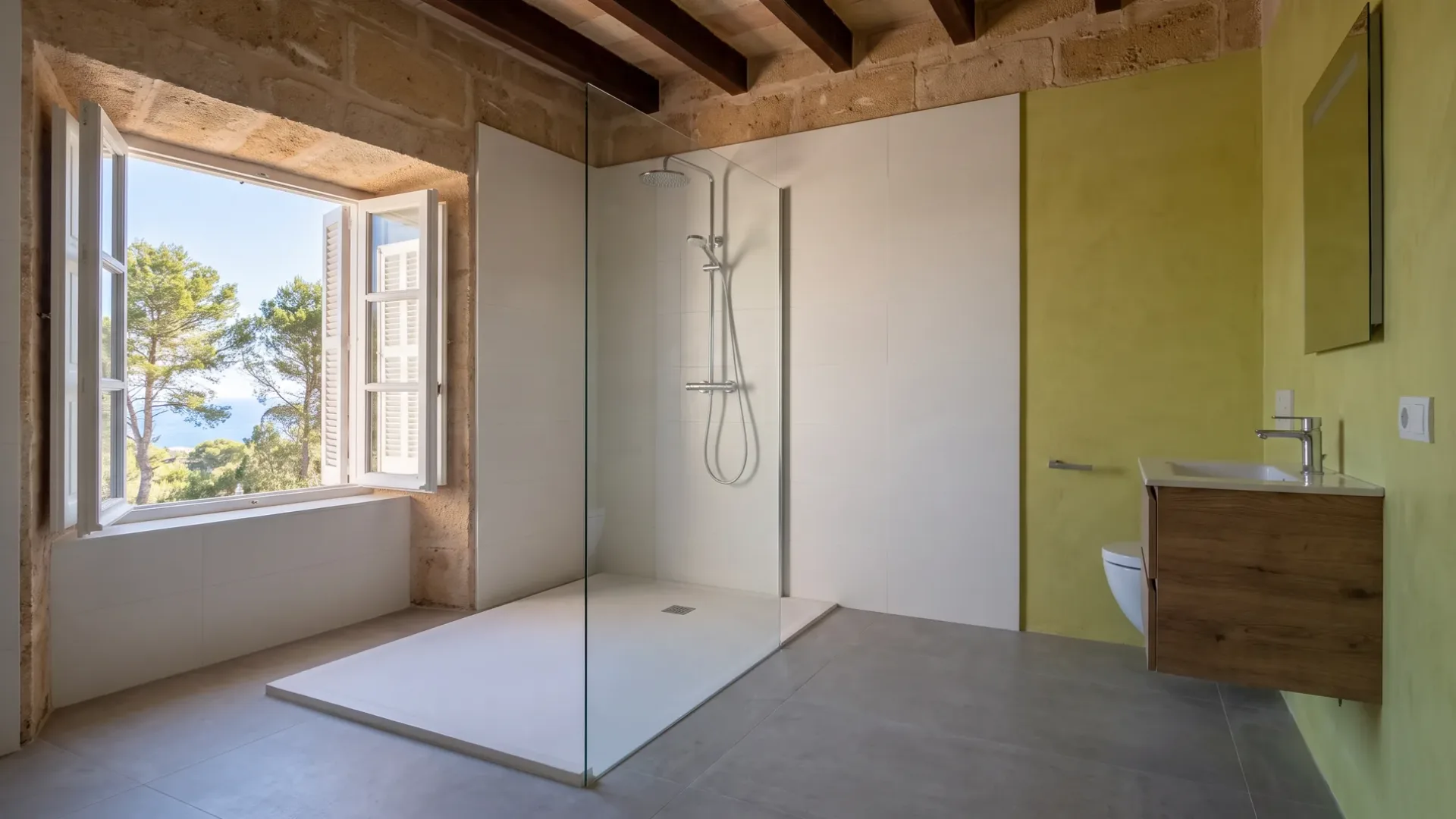Una ducha a ras de suelo con azulejos blancos se sitúa junto a una pared mostaza, un mueble de madera y una ventana enmarcada por pinos y mar.