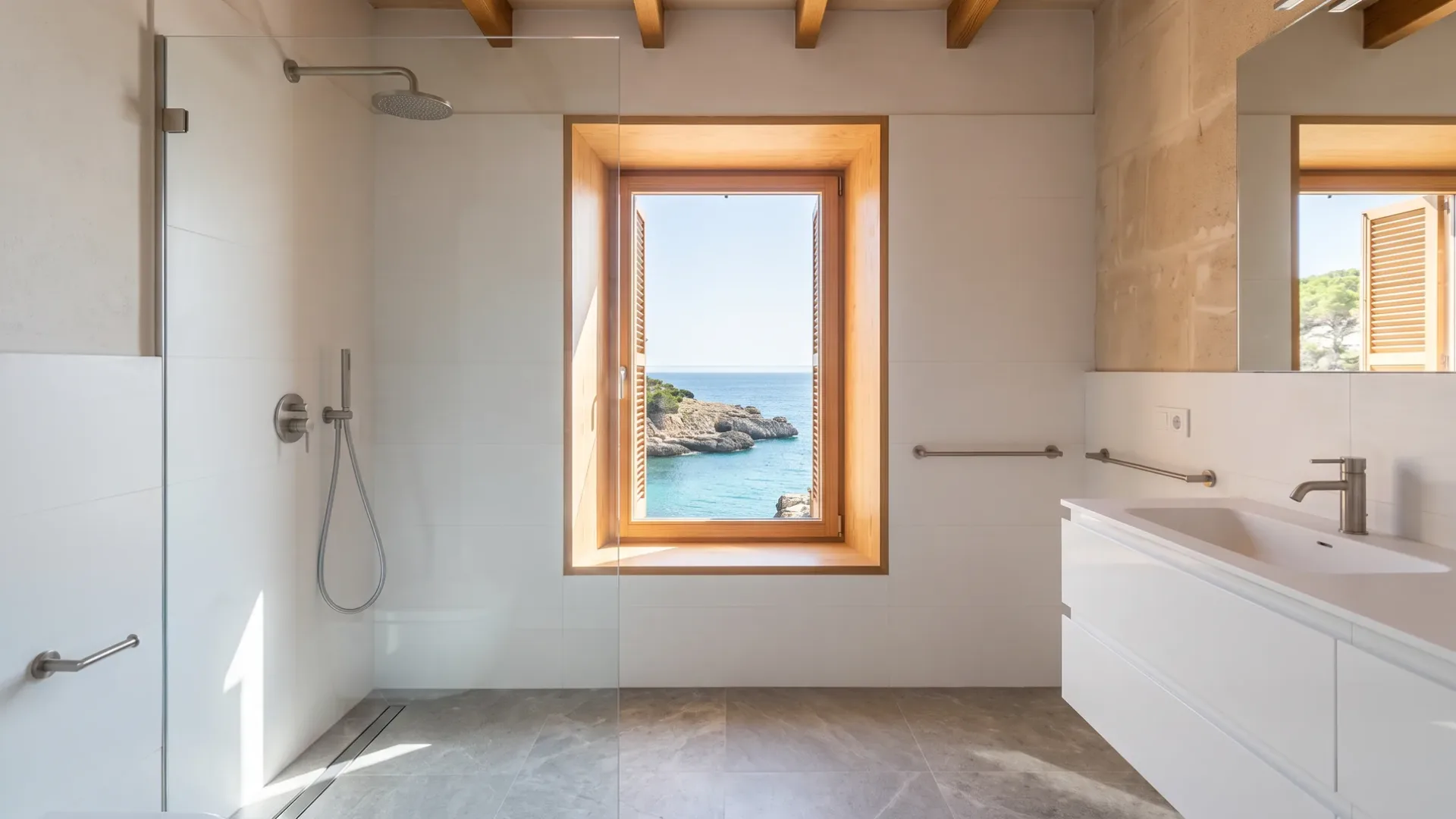 A glass shower with steel fittings faces a timber-framed window, with turquoise water and a rocky coastline beyond.