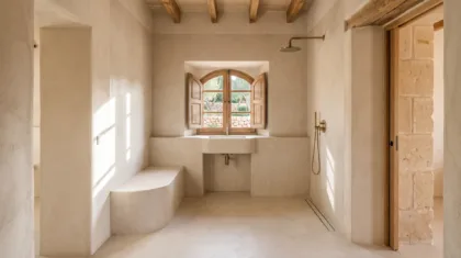 Pale microcement wraps a sunken sink recess below a shuttered window, with a curved bench and open shower to the side.