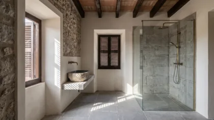 A glass shower with stone-clad walls sits beside a shuttered window, with a stone basin on the opposite wall.