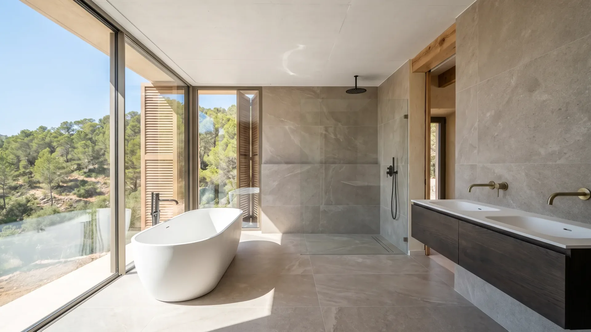 A bathroom with a freestanding oval tub faces glass walls overlooking pine covered hills, beside a dark double vanity.