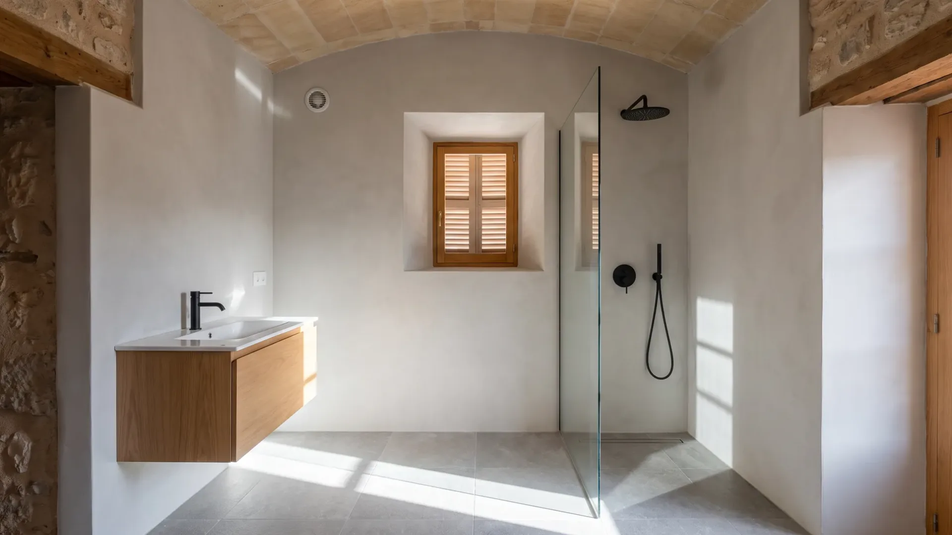 Ein Eichenwaschtisch liegt einem vertieften Fenster mit Fensterläden gegenüber, mit einer Glasdusche und schwarzen Armaturen in der hintersten Ecke.