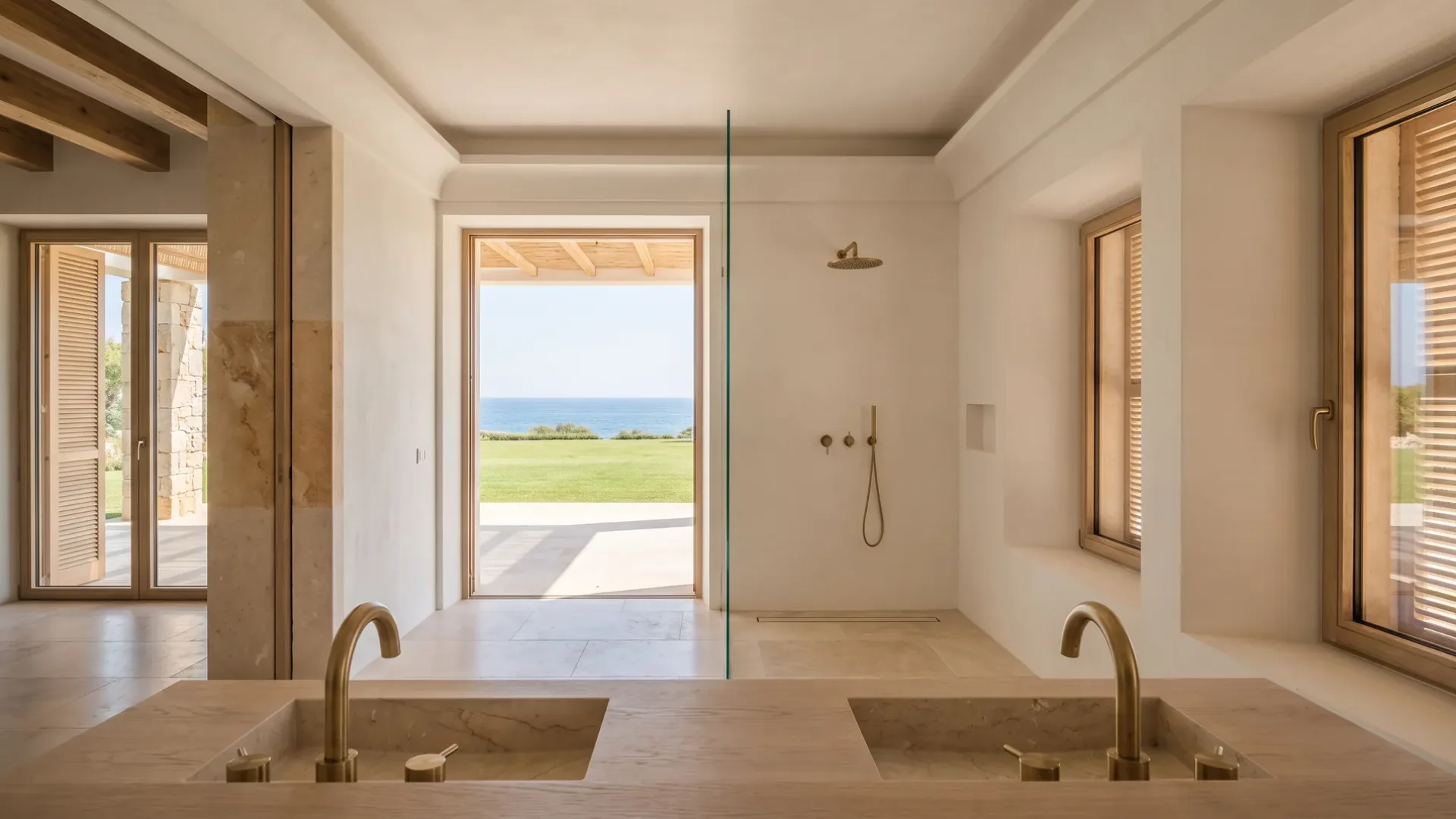 Twin stone trough basins with brass taps sit before an open doorway framing a lawn and the sea beyond.