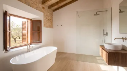A freestanding tub with floor mounted taps sits beneath a window opening onto orchard trees, opposite a glass walk in shower.